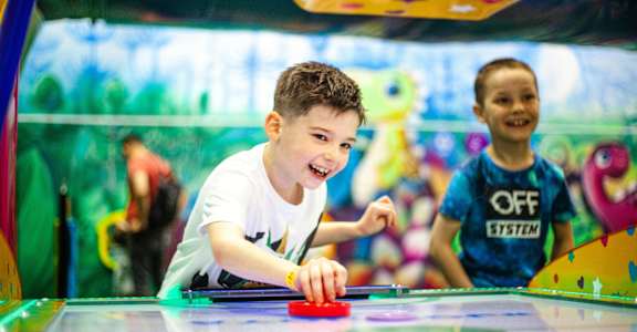 A boy is playing air hockey in a colorful arcade.