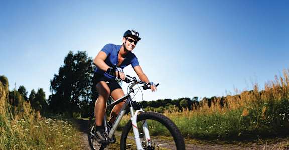 A man in a blue shirt and black shorts is riding a bicycle on a trail.
