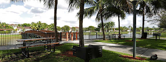 A park with a bench, lamp post and a fence.
