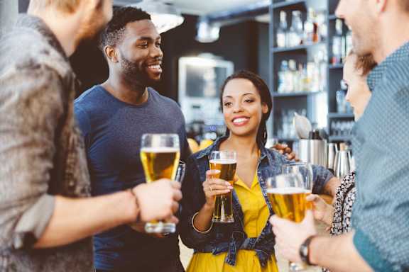 A group of people are toasting with beer glasses in a bar.
