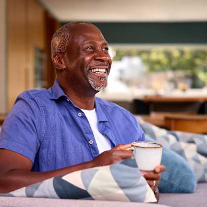 A man in a blue shirt is sitting on a couch holding a cup.