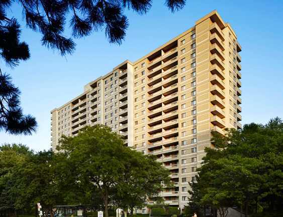 A tall building with balconies is surrounded by trees.