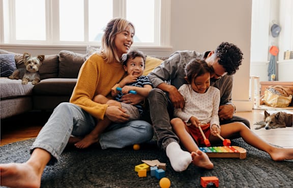 A family of four is playing with toys on the floor in their living room.