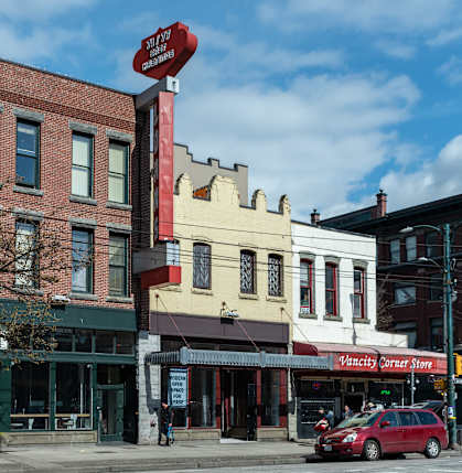 A red car is parked in front of a building with a sign that says Vancity Corner Store.