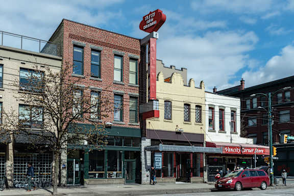 A red car is parked in front of a building with a sign that says Vancity Corner Store.