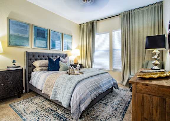 A bedroom with a bed, nightstand, and a wooden table with a lamp on it.