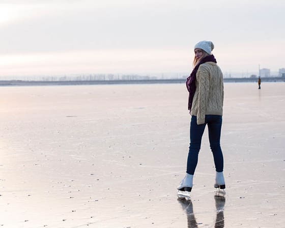 A woman in a white sweater and blue jeans is walking on a beach.