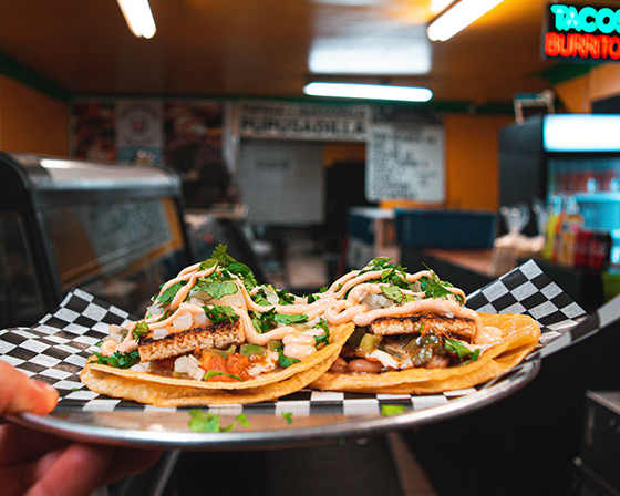 A person is holding a plate with two tacos on a checkered paper.