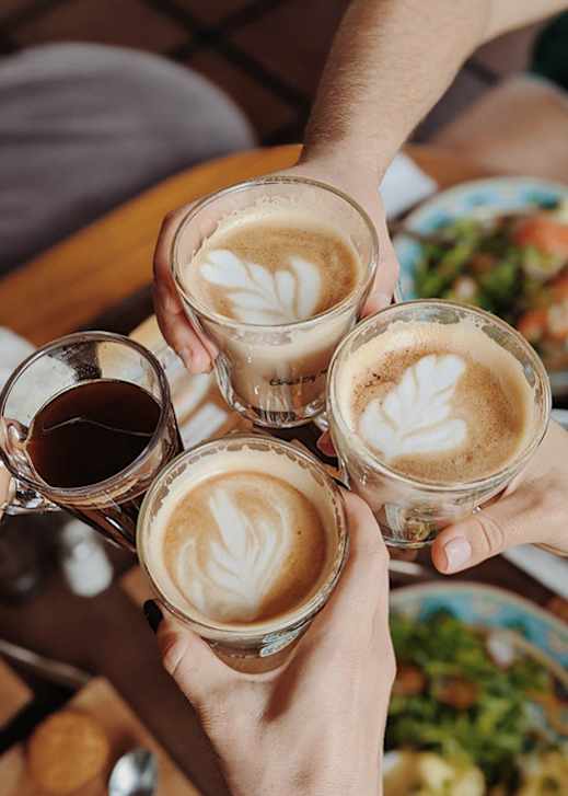 Four hands holding glasses of coffee with latte art.