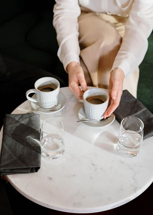 A person is sitting at a table with two cups of coffee and two glasses of water.