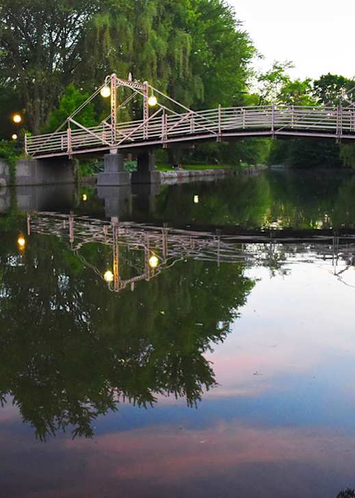 A bridge over a calm body of water with lights on it.