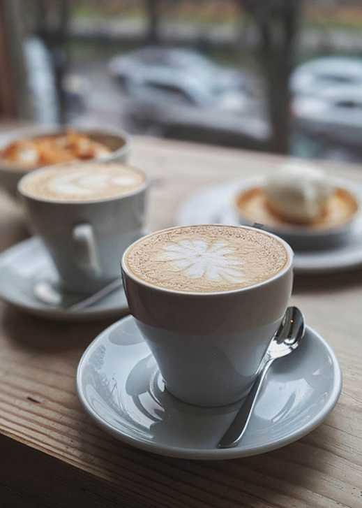 A cup of coffee with a latte art on top is placed on a saucer with a spoon beside it.