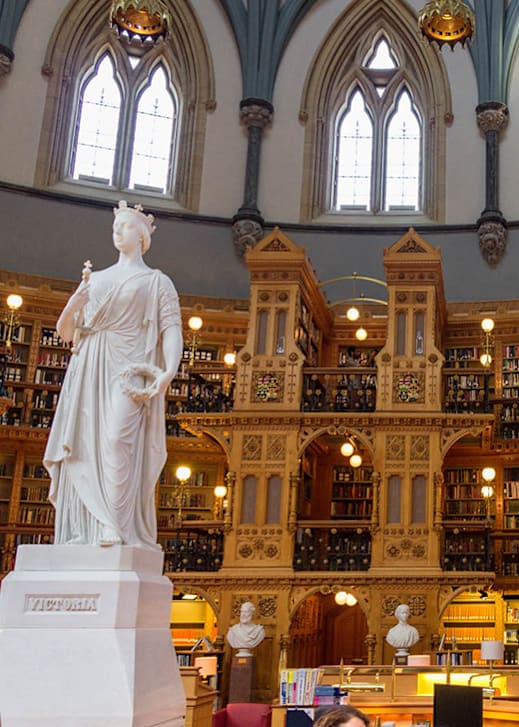 A statue of a woman stands in a library with bookshelves in the background.