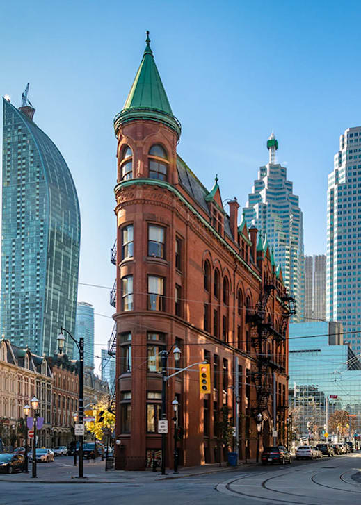 A red brick building with a green roof stands in front of a modern glass building.