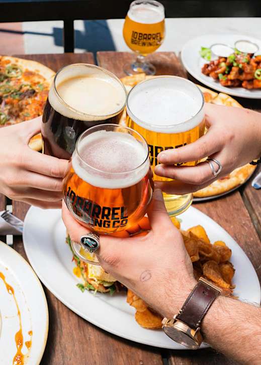 A group of people toasting with beer glasses at a table with food.