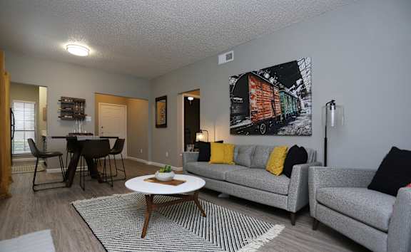 A living room with a grey couch, a coffee table, and a large painting of a train on the wall.