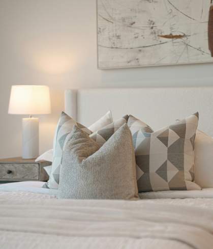 A bed with white pillows and a white headboard with a painting on the wall above it.