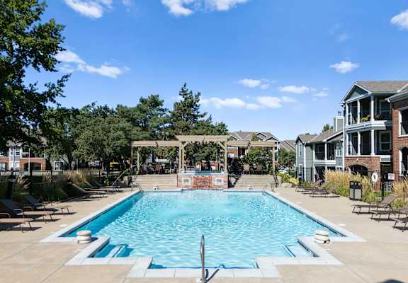 A large swimming pool surrounded by lounge chairs and trees. at Somerset Oaks Apartment Homes, Olathe