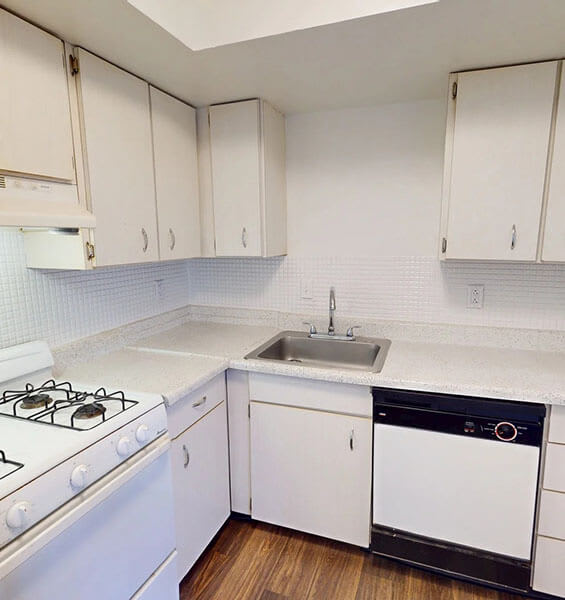 A white kitchen with a stove, sink, and cabinets.