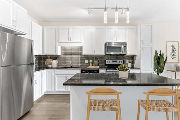 A kitchen with a black countertop and wooden chairs.