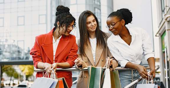Three women examining shopping bags in a city setting.