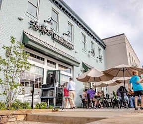 A group of people are sitting outside of a restaurant named The Mart. at Ovation at Town Madison, Madison