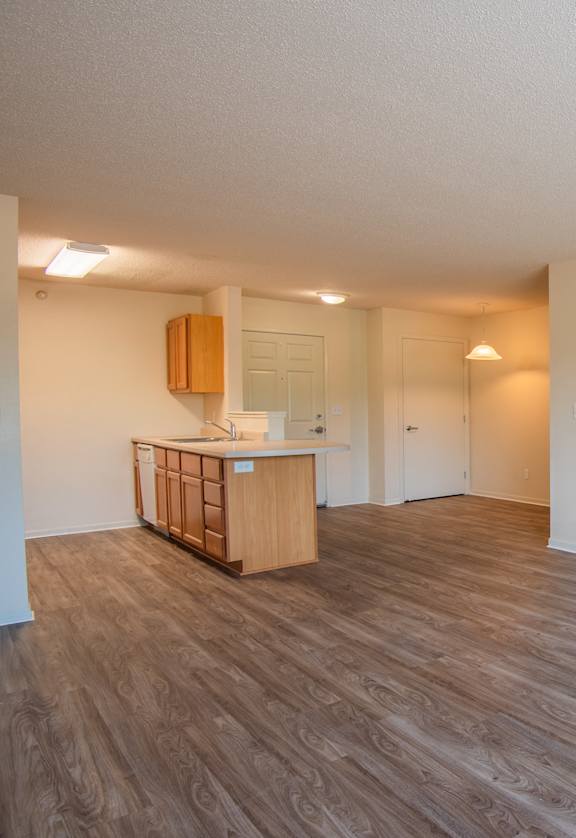 an empty living room and kitchen with wood flooring and white walls