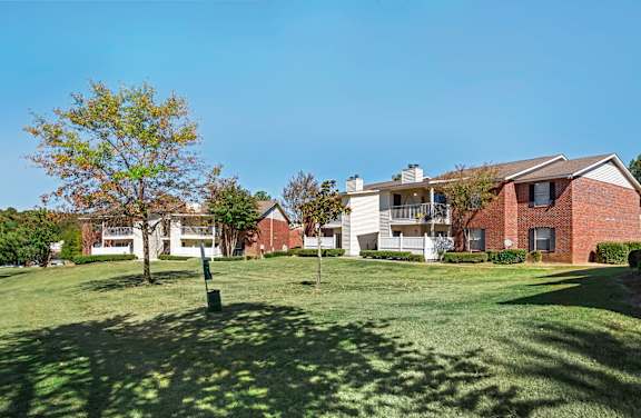 A tree stands in a grassy field in front of apartment buildings.