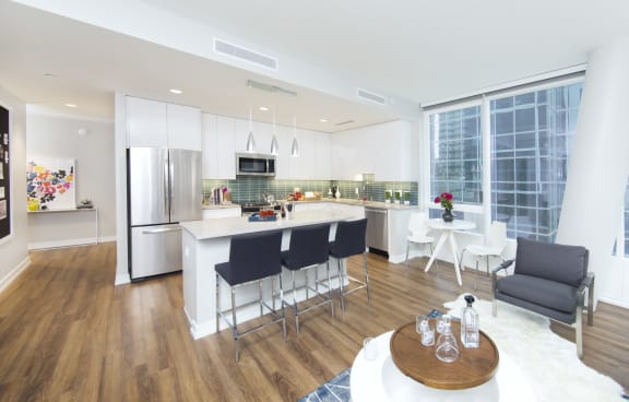 Open kitchen and dining space with hardwood floors, energy efficient stainless steel appliances and quartz countertops. floor to ceiling windows.