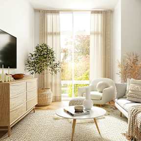 A living room with a grey couch, a white chair, a wooden cabinet, a round mirror, and a flat screen TV.