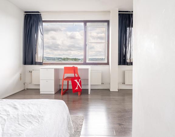 A red chair is in a white room with a large window.