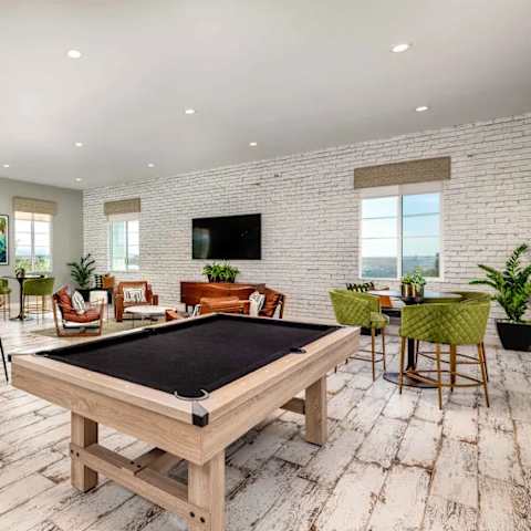 A pool table is in the middle of a room with a brick wall and a television.