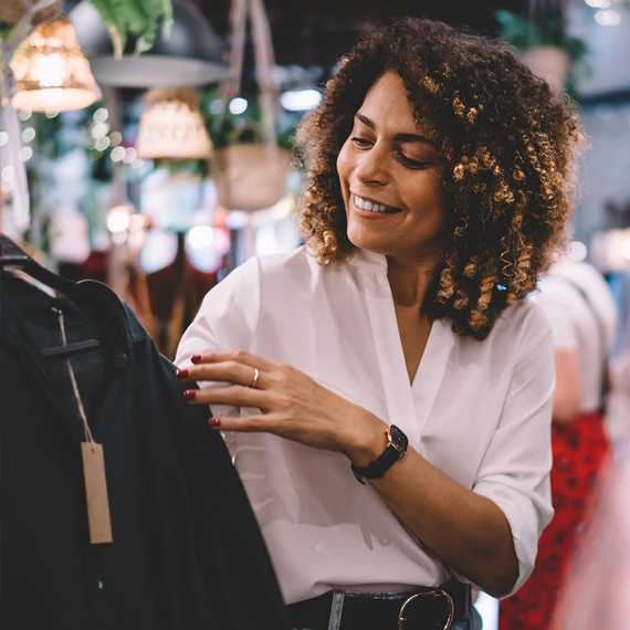 A woman with curly hair is smiling while looking at a black garment.
