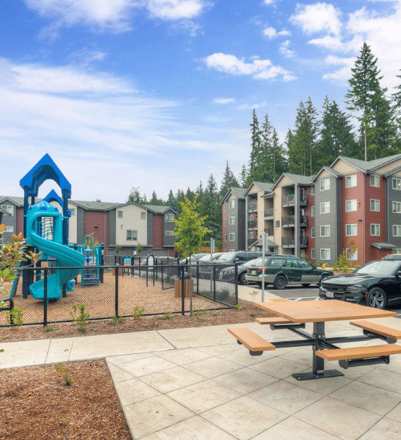 A playground with a blue slide and a picnic table in front of apartment buildings.