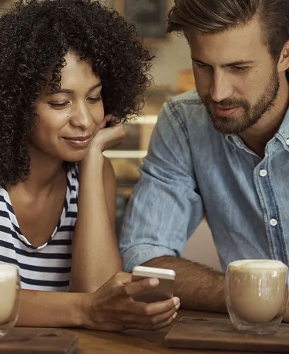 a man and woman sitting at a table looking at a cell phone