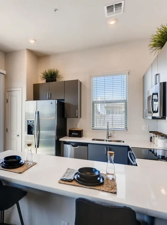 A modern kitchen with a white countertop and black chairs.