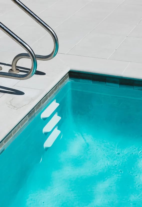 a sparkling blue swimming pool with a stainless steel ladder next to it