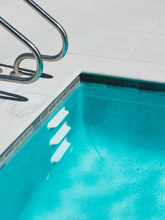a sparkling blue swimming pool with a stainless steel ladder next to it