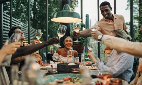 a group of people sitting around a dinner table drinking wine