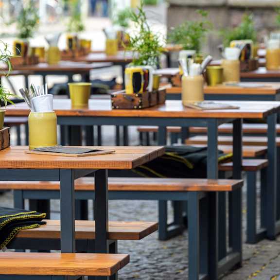 A row of tables with yellow cups and green plants on them.