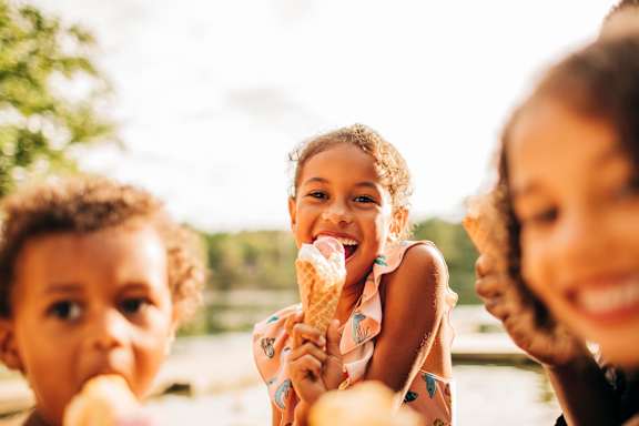 Three children eating ice cream in a sunny outdoor setting.