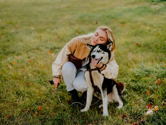A woman is hugging a husky dog in a field.