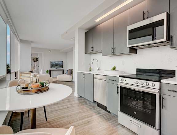 A modern kitchen with a white table and chairs, a microwave above the stove, and a view of the ocean through the window.