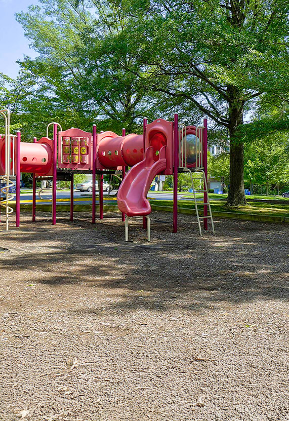 A red slide in a playground surrounded by trees.