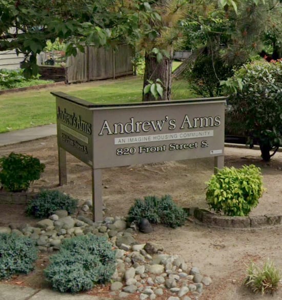 A sign for Andrew's Arms housing community stands in front of a garden.