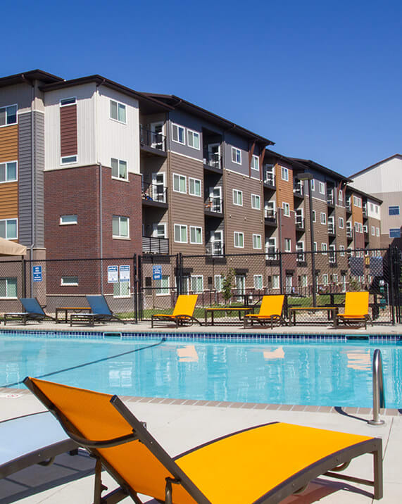 a swimming pool with yellow chaise lounge chairs in front of an apartment building