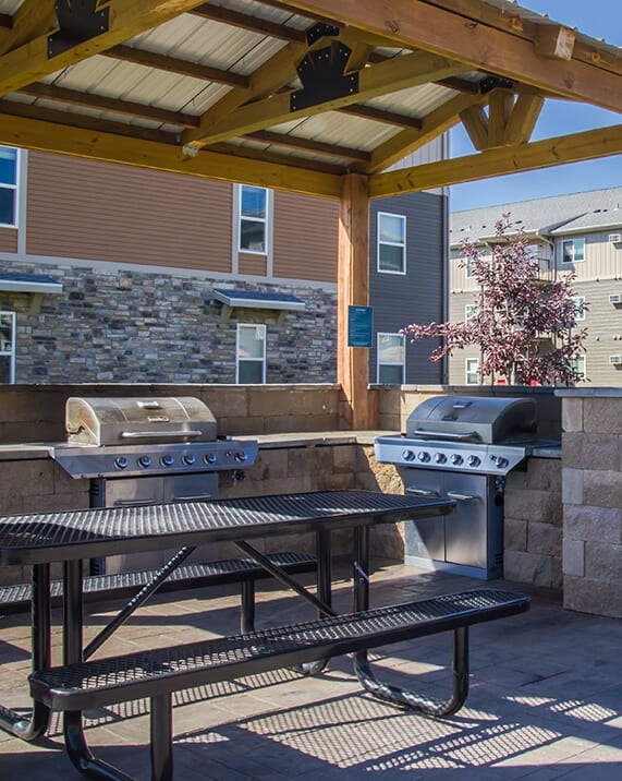a pergola with a grill and picnic table in front of a stone wall