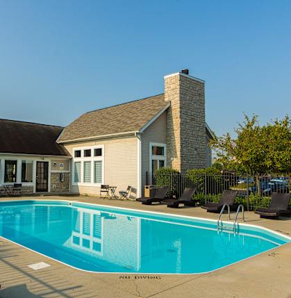 A pool with lounge chairs and a house in the background.