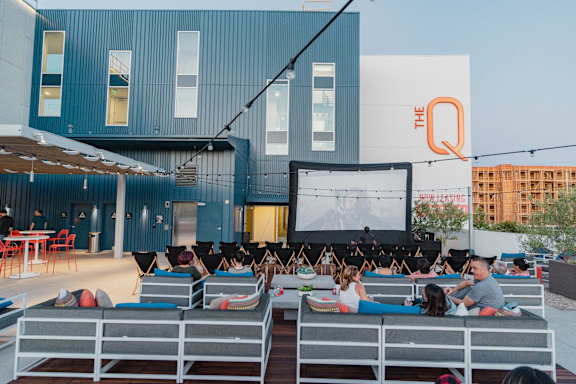 A group of people are sitting on lounge chairs and watching a movie on a large screen.