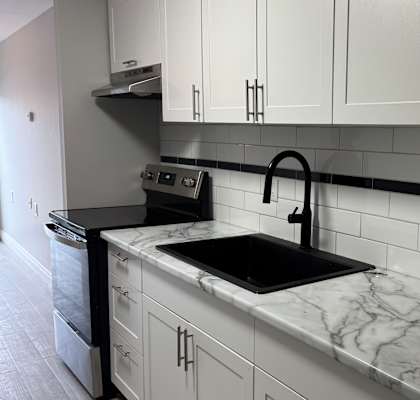 A kitchen with white cabinets and a black and white tiled backsplash.